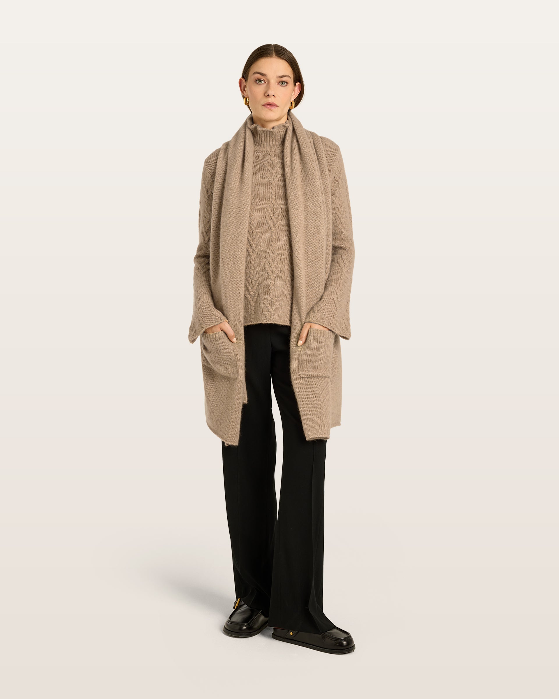 Damen Pullover aus 75 % Kaschmir und 25 % Seide in Warm Sand – Pullover mit klassischem Zopfmuster in mittelschwerer Qualität und figurbetonter A-Linien-Silhouette. Der schmale, hohe Kragen mit Rollkante sowie die langen, ausgestellten Ärmel verleihen dem Modell eine feminine und elegante Ausstrahlung.
