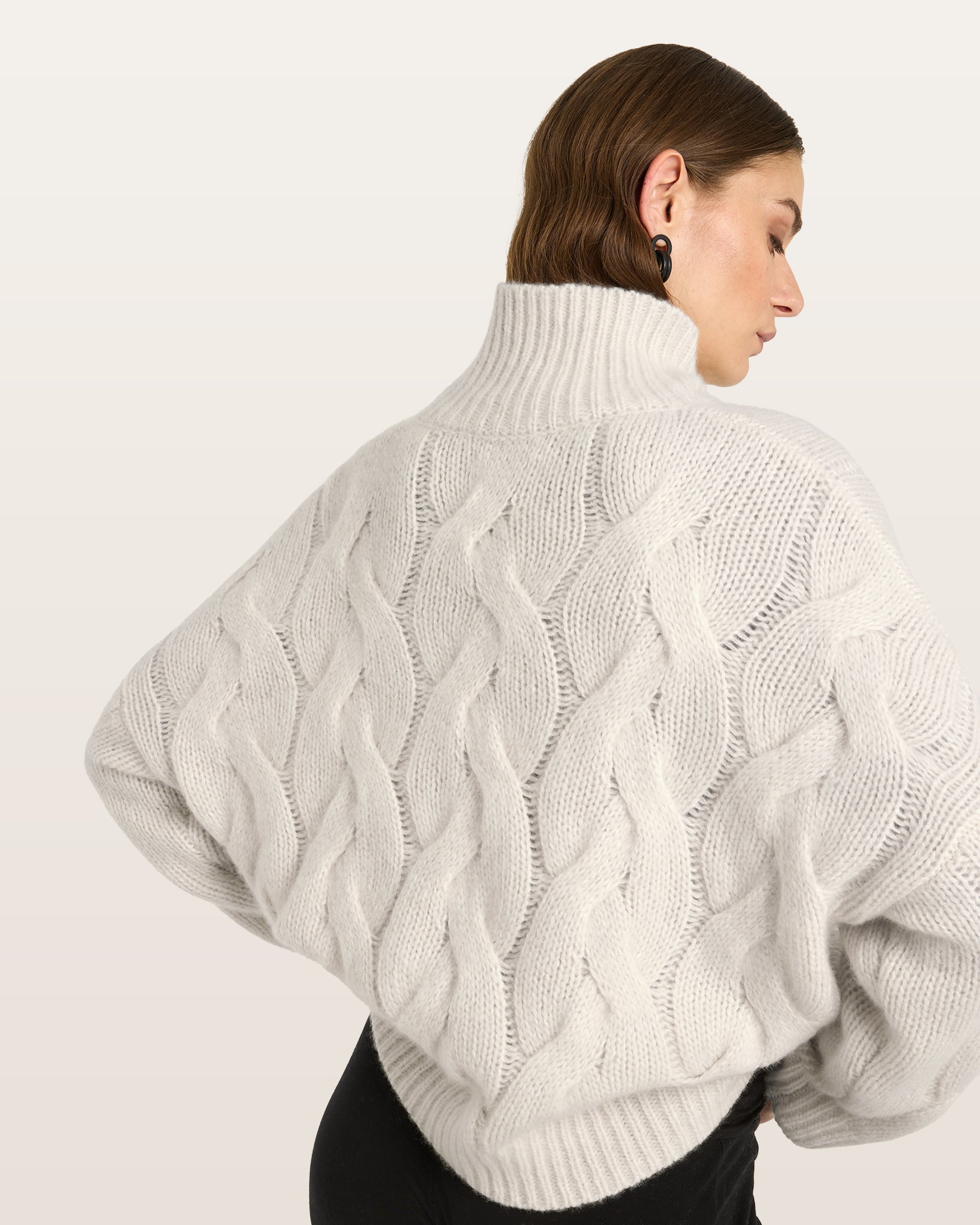 Damen Pullover aus 75 % Kaschmir und 25 % Seide in Ivory – grob gestrickter Pullover mit Zopfstrickmuster in oversized Passform mit langer, weiter Silhouette. Das Modell verfügt über einen hohen Stehkragen in Rippstruktur, eine überschnittene Schulter sowie lange, weite Ärmel. Ärmelbündchen und Saum sind in Rippstruktur gearbeitet und unterstreichen den markanten Strickcharakter des Designs.