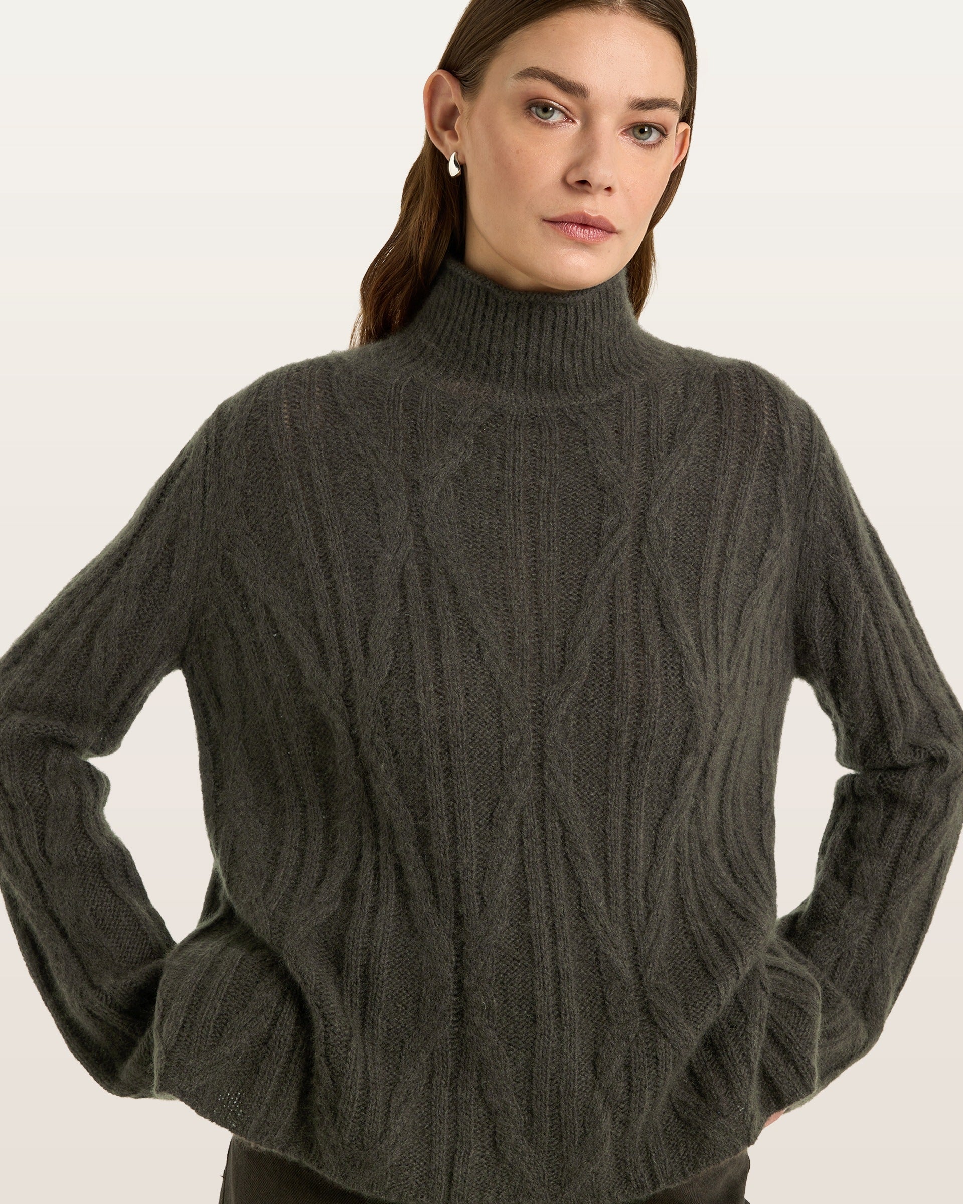 Damen Pullover aus 75 % Kaschmir und 25 % Seide in Black Forest – Pullover mit Zopfmuster in mittelschwerer Strickqualität und figurbetonter A-Linien-Passform, schmalem, hohem Kragen in Rippstruktur mit Rollkante sowie langen, relaxten Ärmeln. Das Modell verbindet markante Strickdetails mit einer femininen, leicht ausgestellten Silhouette.
