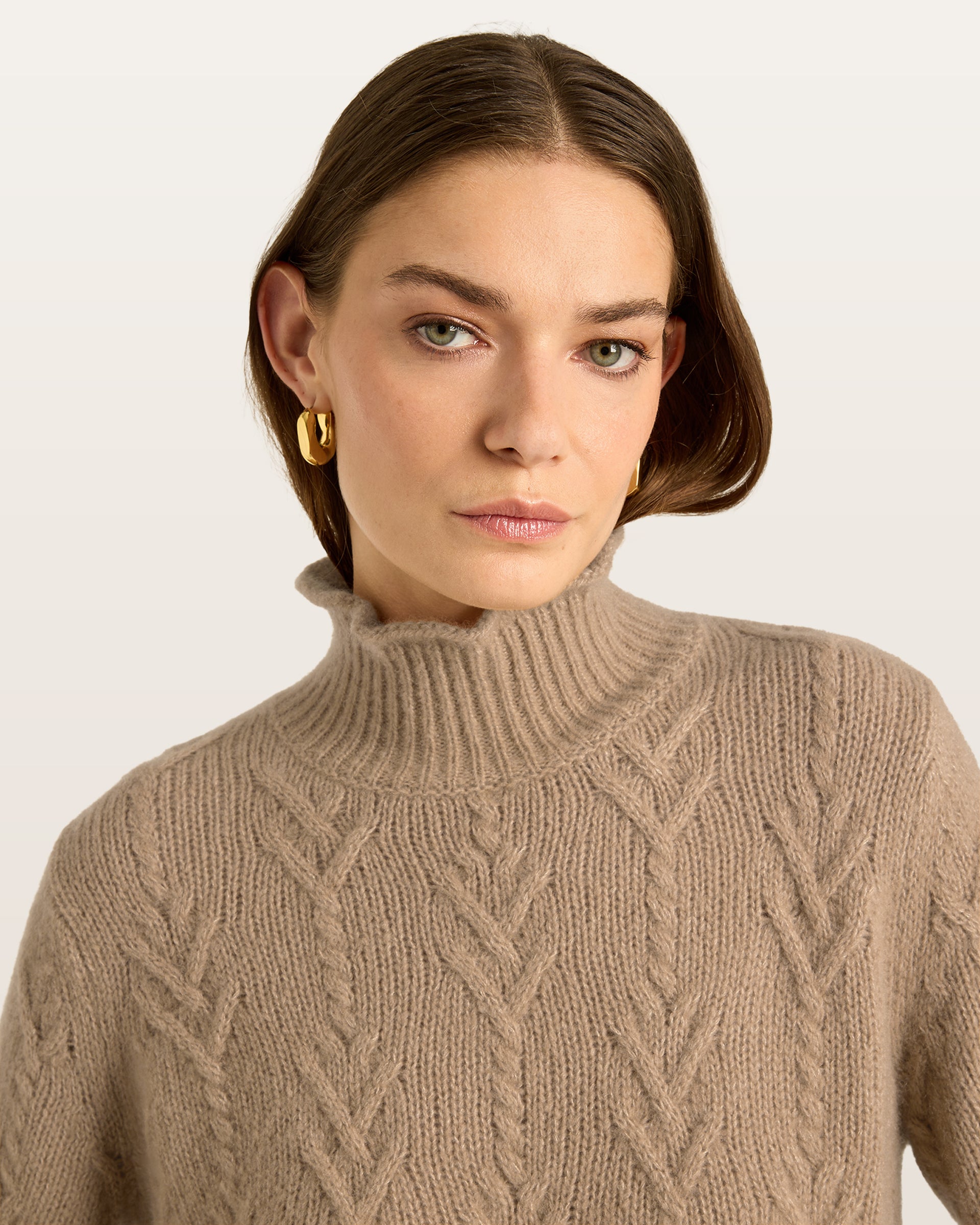 Damen Pullover aus 75 % Kaschmir und 25 % Seide in Warm Sand – Pullover mit klassischem Zopfmuster in mittelschwerer Qualität und figurbetonter A-Linien-Silhouette. Der schmale, hohe Kragen mit Rollkante sowie die langen, ausgestellten Ärmel verleihen dem Modell eine feminine und elegante Ausstrahlung.