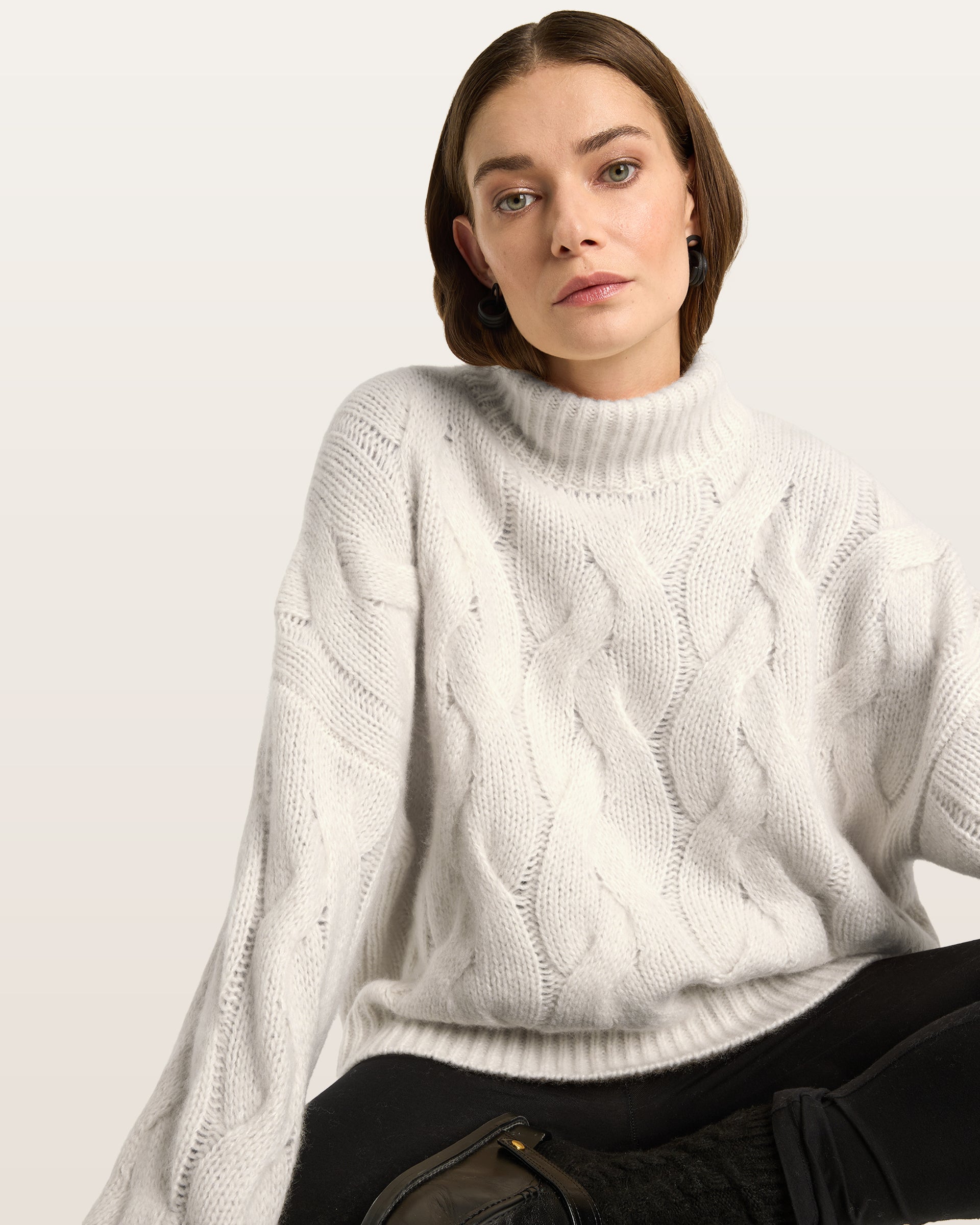 Damen Pullover aus 75 % Kaschmir und 25 % Seide in Ivory – grob gestrickter Pullover mit Zopfstrickmuster in oversized Passform mit langer, weiter Silhouette. Das Modell verfügt über einen hohen Stehkragen in Rippstruktur, eine überschnittene Schulter sowie lange, weite Ärmel. Ärmelbündchen und Saum sind in Rippstruktur gearbeitet und unterstreichen den markanten Strickcharakter des Designs.